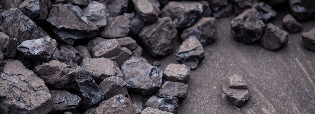 Steinkohlebrocken liegen unregelmäßig auf einer grauen Oberfläche verteilt. Diese Kohlenstücke sind von unterschiedlicher Größe und scheinen roh und unpoliert zu sein. Energiequelle und Heizmaterial relevant.