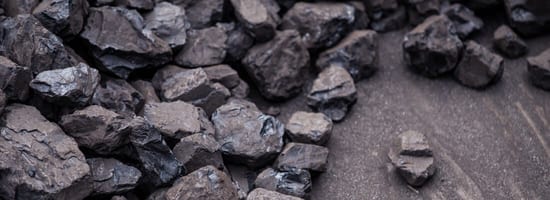 Steinkohlebrocken liegen unregelmäßig auf einer grauen Oberfläche verteilt. Diese Kohlenstücke sind von unterschiedlicher Größe und scheinen roh und unpoliert zu sein. Energiequelle und Heizmaterial relevant.