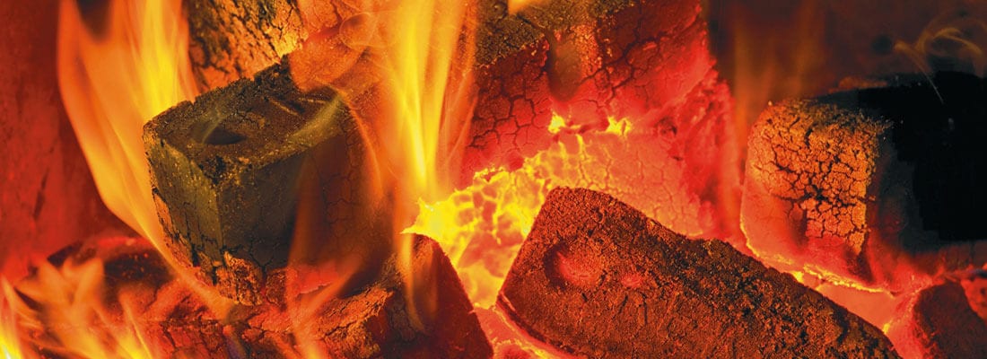 Glühende Holzbriketts lodern mit intensiven Flammen in einer Feuerglut. Die brennenden Briketts erzeugen eine warme, angenehme Atmosphäre, die ideal für gemütliche Abende ist.