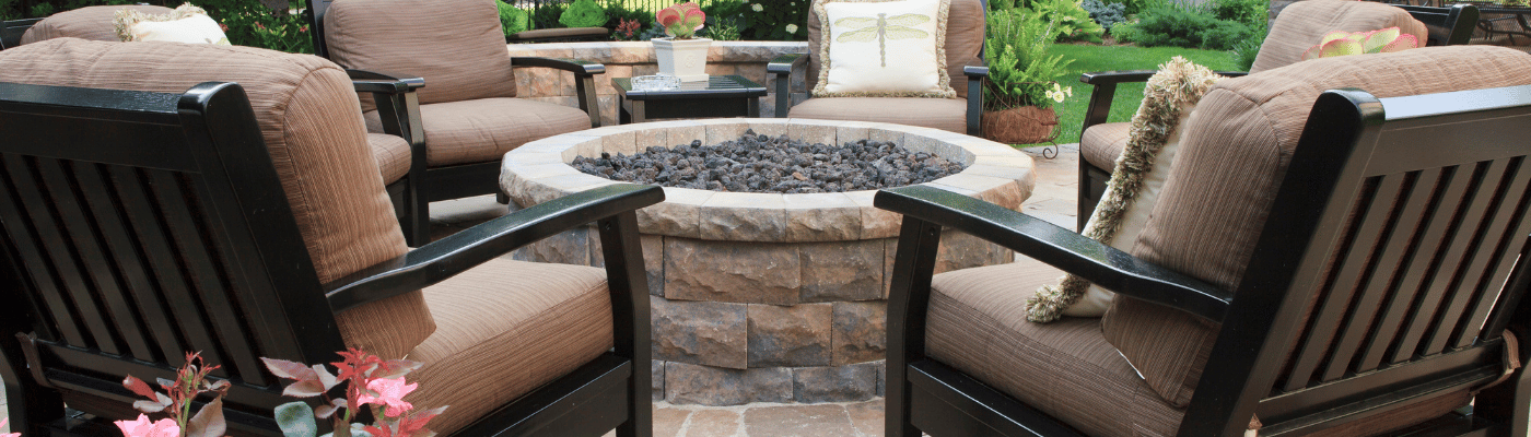 Eine gemütliche Sitzecke im Garten mit Stühlen und einem kleinen Feuerstellen-Tisch in der Mitte.